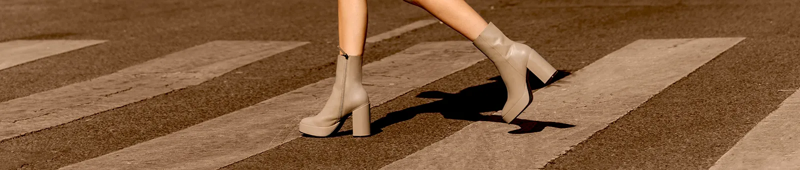 A person wearing beige platform boots walks across a zebra crossing on an asphalt road.