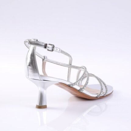 Silver strappy high-heeled sandal with rhinestone-embellished straps and a short curved heel on a reflective surface