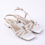 White braided-strap sandals with a low block heel and gold buckle, featuring jeweled seahorse ornaments on the straps.