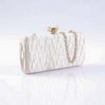 White textured clutch purse with a gold chain strap lying on a reflective surface near a pale background.