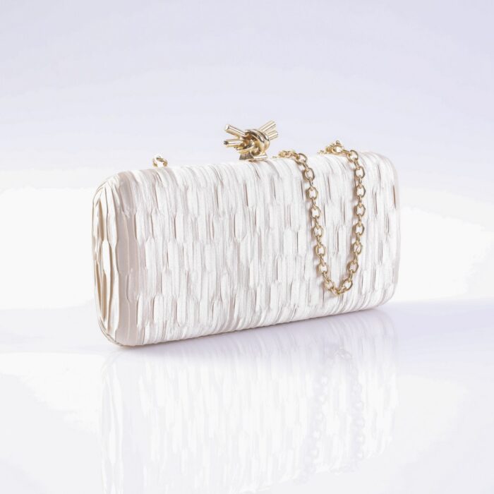 White textured clutch purse with a gold chain strap lying on a reflective surface near a pale background.