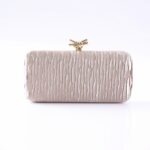 Beige quilted clutch purse with a gold knot clasp, resting on a white surface.