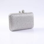 Silver rhinestone-encrusted clutch purse with a beaded ball clasp on a reflective surface