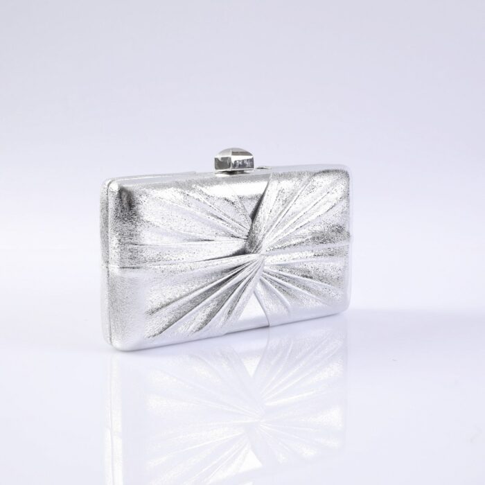 Silver rectangular clutch purse with a starburst embossed pattern and a small rounded clasp on top, photographed against a pale background with a reflective surface
