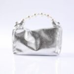 Silver metallic clutch with a pearl bead handle, resting on a white reflective surface.