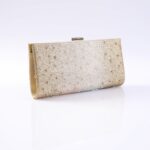 Gold clutch purse covered in rhinestones with a metal clasp on top, resting on a reflective white surface.