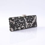 Black lace evening clutch with a metallic clasp, resting on a reflective white surface and subtle shadowing.