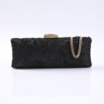 Black lace evening clutch with a gold-toned chain strap and angular clasp on a white reflective surface