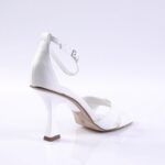 White open-toe sandal with ankle strap and curved high heel on a white backdrop﻿.