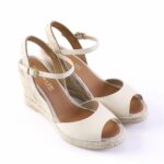 Beige peep-toe wedge sandals with ankle straps and rope-wrapped sole on a white background