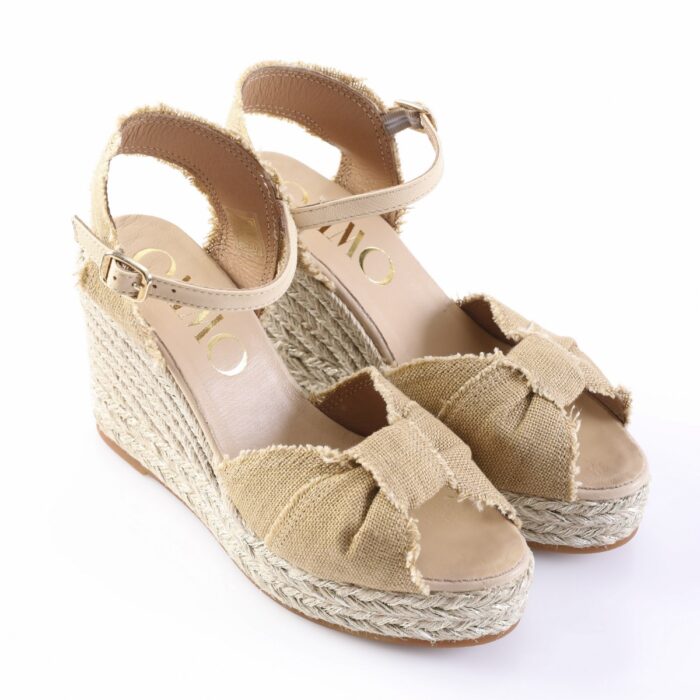 Beige fabric wedge espadrille sandals with braided jute sole, bow accents on the toe, and an ankle strap with a buckle.