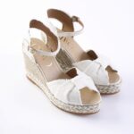 White fabric wedge espadrille sandals with braided jute sole and ankle straps, viewed from a slight angle for detail and texture.