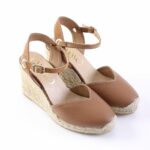 Brown leather wedge sandals with ankle straps and braided jute platform, shown from a side angle on white background on a sunny day aesthetic.