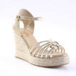 Gold wedge sandal with braided jute sole, knotted front straps, and ankle strap with buckle.