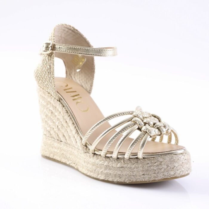 Gold wedge sandal with braided jute sole, knotted front straps, and ankle strap with buckle.