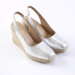 Silver wedge espadrille slingback sandals with woven rope platform and open toe, viewed from above-right angle, brand not fully visible.