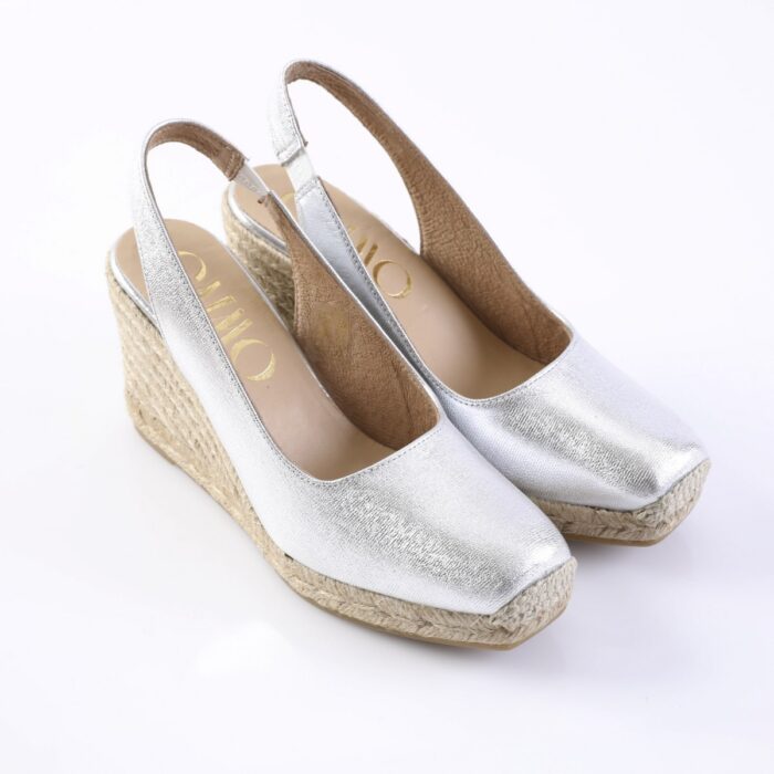 Silver wedge espadrille slingback sandals with woven rope platform and open toe, viewed from above-right angle, brand not fully visible.