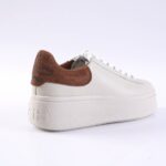 White platform sneaker with a brown suede heel counter and decorative stud pattern on the back; white laces and a chunky textured sole.