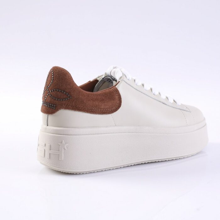 White platform sneaker with a brown suede heel counter and decorative stud pattern on the back; white laces and a chunky textured sole.