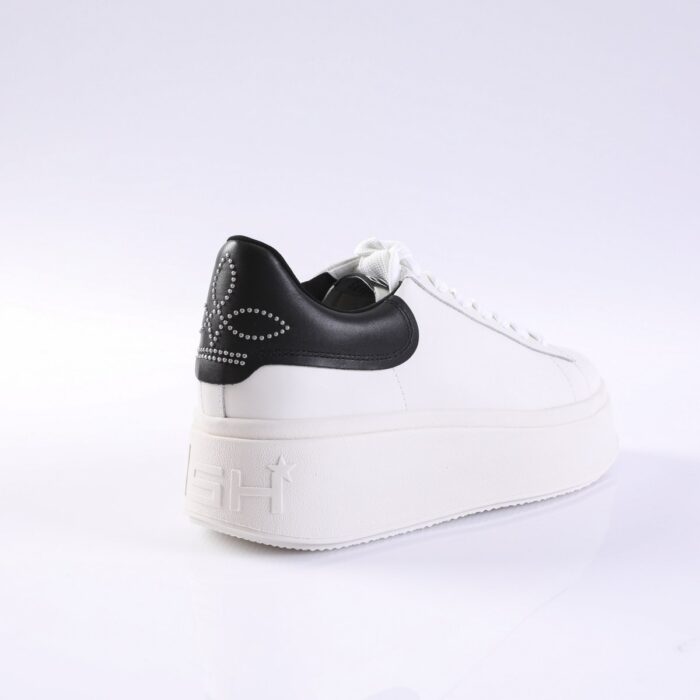 White platform sneaker with a black studded heel patch and white laces, shown in three-quarter rear view.