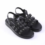 Black open-toe sandals with multiple metal eyelets and decorative cutouts on a low platform sole.