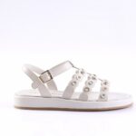 White sandal with decorative circular metal embellishments along the straps and an adjustable buckle strap, flat sole