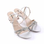 Silver strappy high-heeled sandals with knotted front straps against a white background.