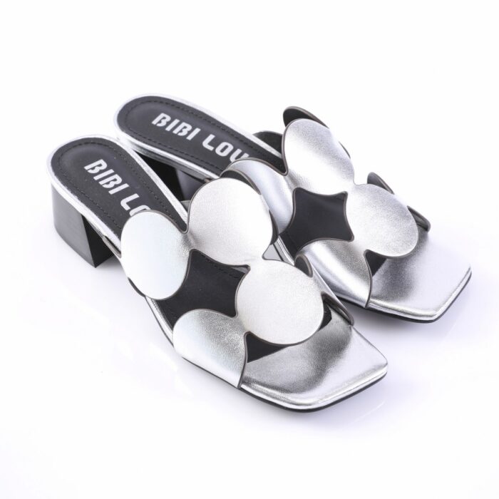 Silver metallic open-toe slide sandals with oversized flower-shaped appliqués and a chunky black block heel on a white background.