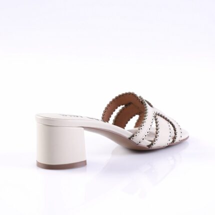 White open-toe mule with scalloped cutout straps and a chunky low heel on a reflective surface