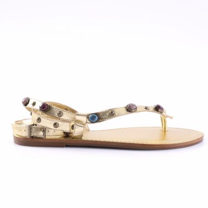 Gold strappy flat sandal with metal studs and multicolor gemstone accents, buckle at the heel strap.
