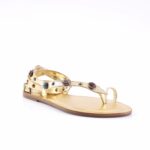 Gold-toned flat sandal with studded strap and colored gem accents, thong-style toe loop, low-profile heel.