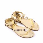 Gold strappy sandals with studded straps and colorful gem accents on a white background.