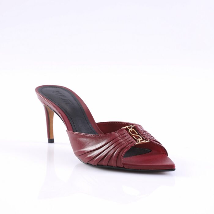 Red mule sandal with pleated front strap and gold chain embellishment, mid-height stiletto heel, on a white reflective surface.