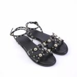 Black studded flat sandals with ankle straps and decorative metal beads, open toe design.