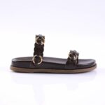 Black flat sandal with two leather straps and gold circular buckles on a tan sole, shown from the side on a white surface
