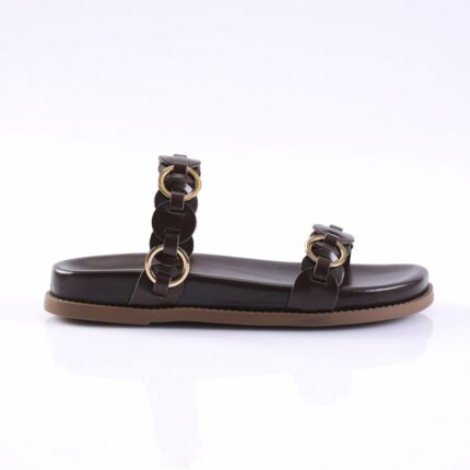 Black flat sandal with two leather straps and gold circular buckles on a tan sole, shown from the side on a white surface