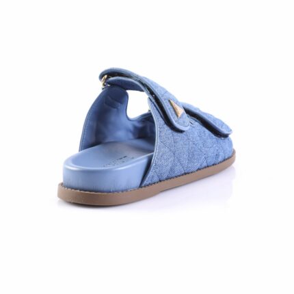 Blue denim slide sandal with open back, brown sole, shown from a rear-side angle.