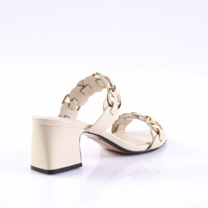 Beige heeled sandal with braided straps and gold chain details on a white reflective surface.