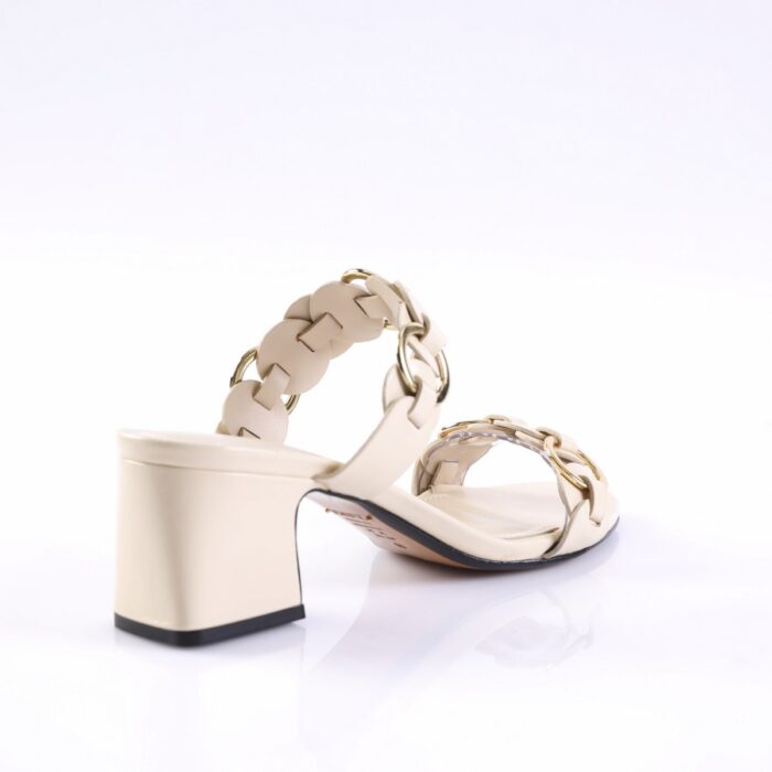 Beige heeled sandal with braided straps and gold chain details on a white reflective surface.