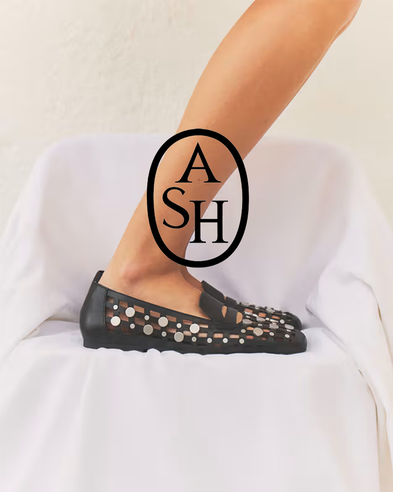 Close-up of a woman's foot in a black perforated flat shoe with circular cutouts, resting on a white surface.
