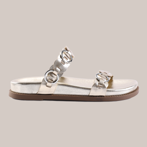Silver flat sandal with two straps and circular chain-link details, on a light beige background.