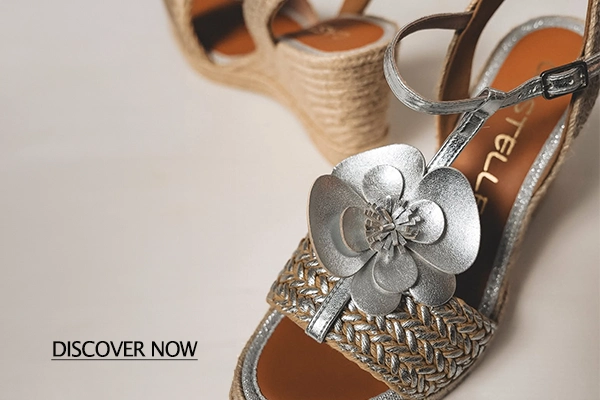 Silver flower embellishment on a woven-strap sandal with a tan insole and metallic details, suitable for a fashion product image under 'Discover Now' promo text in the corner.
