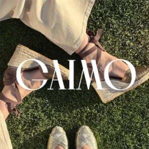Brand advertisement showing two pairs of wedge espadrille sandals on grass with GAIMO in white typography across the image.