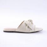 Cream-colored slide sandal with a twisted knot strap across the top and a flat sole.