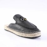 Black leather moccasin-style espadrille with a braided rope sole and metal hardware detail on the vamp, photographed from a side angle for product view
