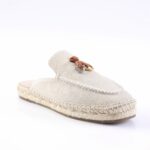 Beige canvas espadrille mule with braided jute sole and decorative brown leather strap with metal rings on the top.