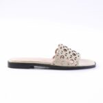 Beige women's slide sandal with a perforated geometric cutout strap and black outsole on a light insole.
