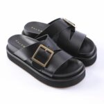 Black platform sandals with two wide crisscross straps and a gold square buckle on the front strap, on a white background