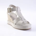 White wedge sandal with crisscross straps and a gold buckle, featuring a woven espadrille heel and a white platform sole.