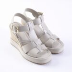 White wedge sandals with multiple straps and gold buckles, espadrille-style heel.